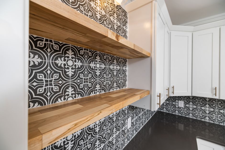 Elegant empty wooden shelves in a modern kitchen with stylish black and white patterned backsplash.